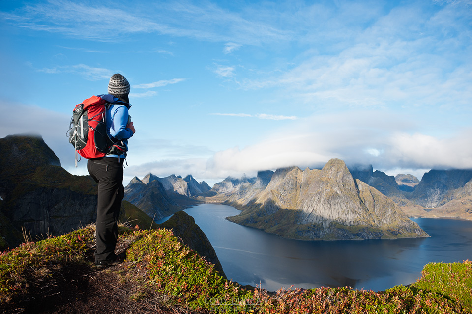 Female hiker enjoys spectacular view over mountains and fjords from Reinebringen, Lofoten islands, Norway