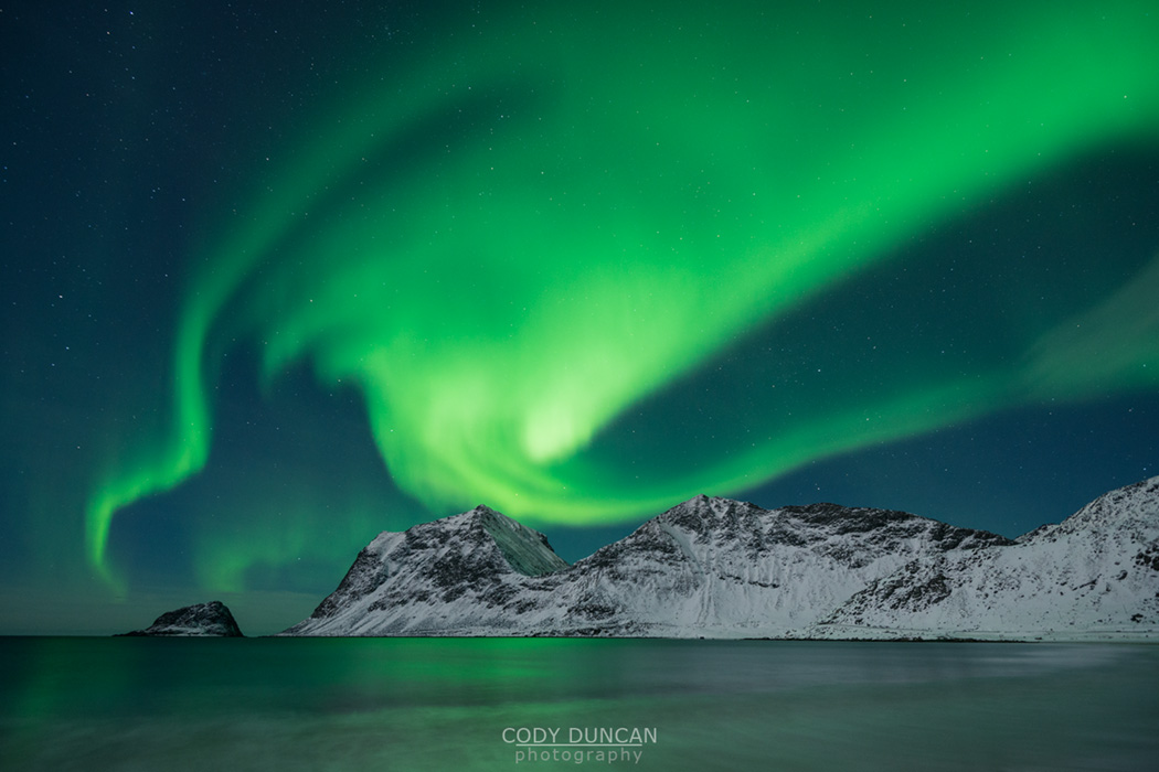 Aurora Borealis - Northern Lights shine in sky over snow covered mountains from Vik beach, Vestvågøy, Lofoten Islands, Norway