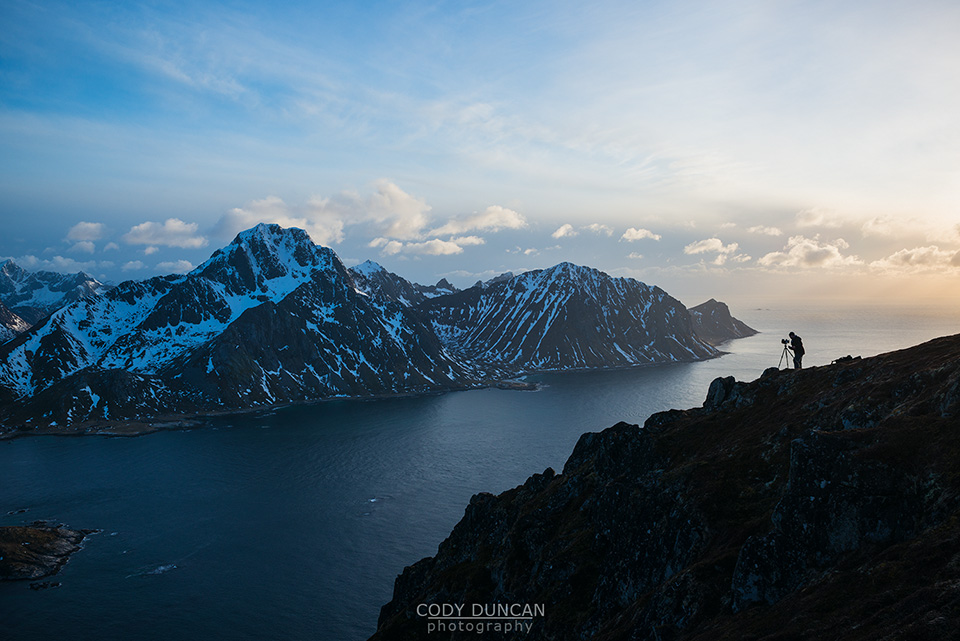 photographer on summit of Offersoykammen with Flakstadoy in background, Lofoten Islands, Norway