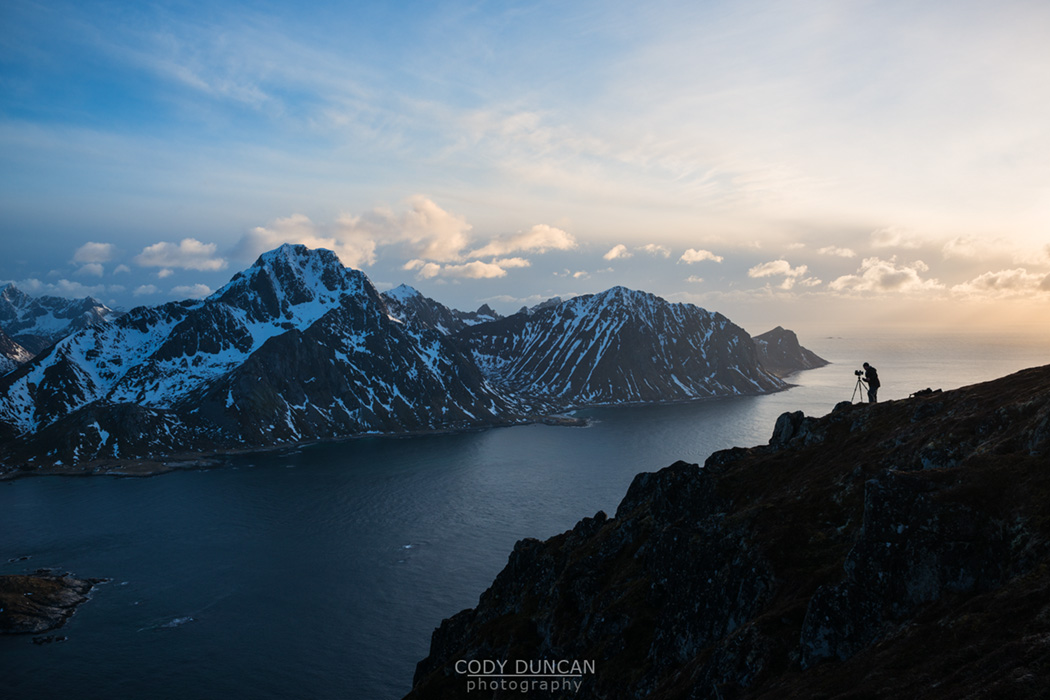 Silhouette of landscape photographer on summit of Offersoykammen with Flakstadoy in background, Lofoten Islands, Norway