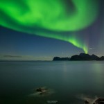 Northern Lights shine in sky over sea and mountains of Vestvagoy, from near Myrland, Lofoten Islands, Norway