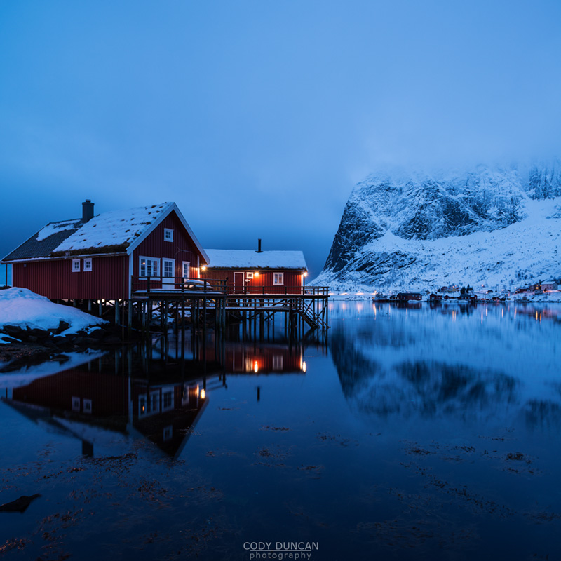 Traditional Rorbu cabin reflects in fjord in evening light, Valen, Reine, Moskenesøy, Lofoten Islands, Norway