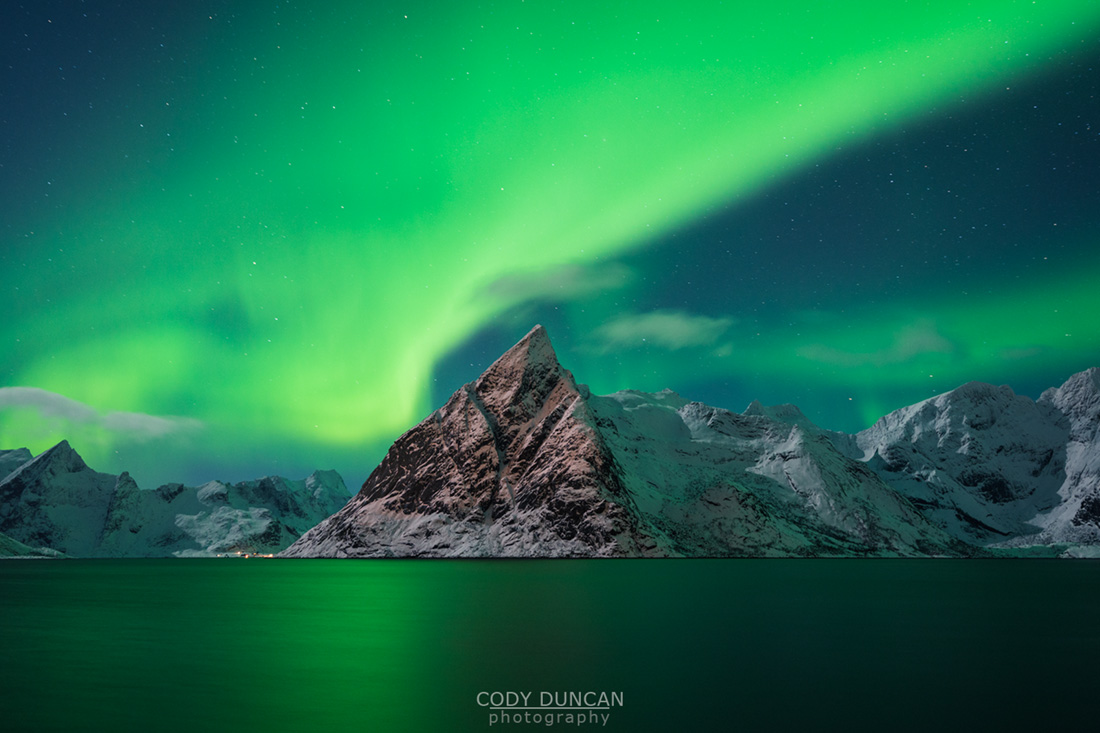 Aurora Borealis - Northern Lights fill sky over Olstind mountain peak and reflect in fjord, Toppøya, Lofoten Islands, Norway