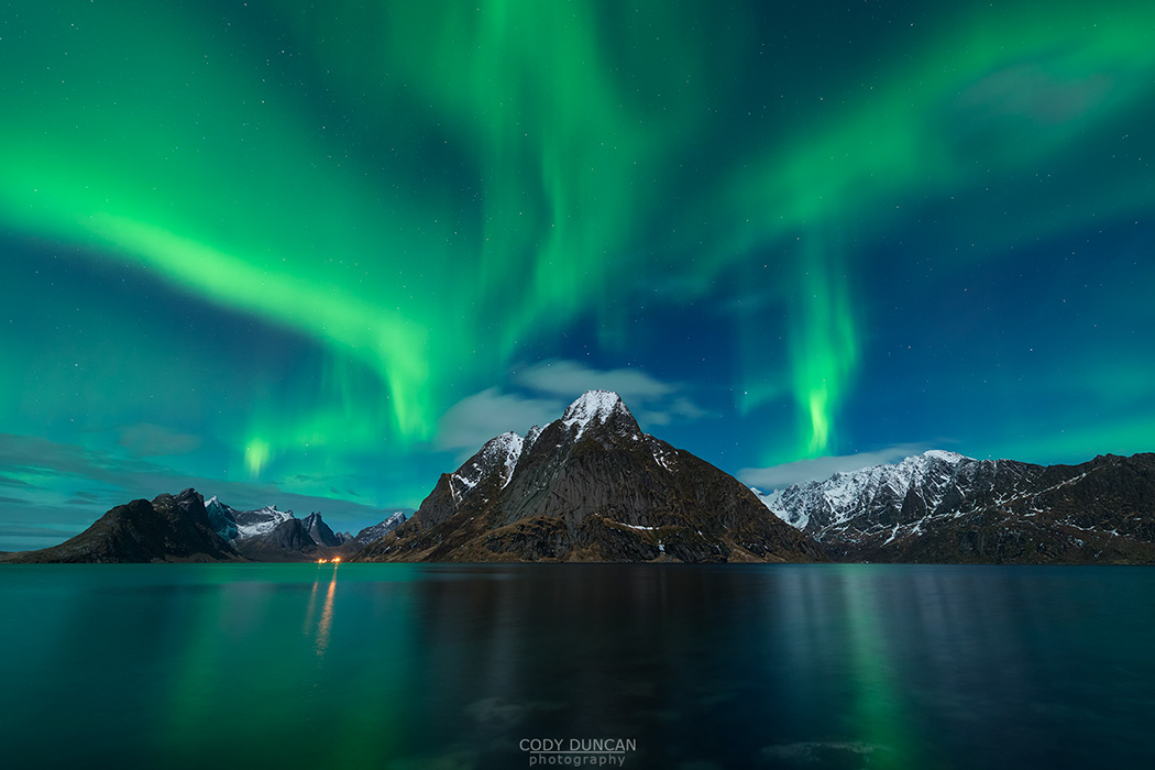 Northern Lights - Aurora Borealis shine in sky over Olstind mountain peak and fjord near Reine, Moskenesøy, Lofoten Islands, Norway