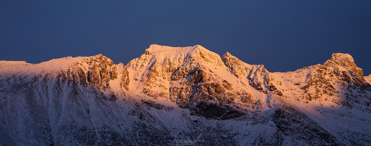 Winter sunset illuminates snow covered mountain peaks, Flakstadøy, Lofoten Islands, Norway