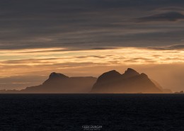 Værøy islands rise over sea while illuminated by winter sunset, Moskenesøy, Lofoten Islands, Norway