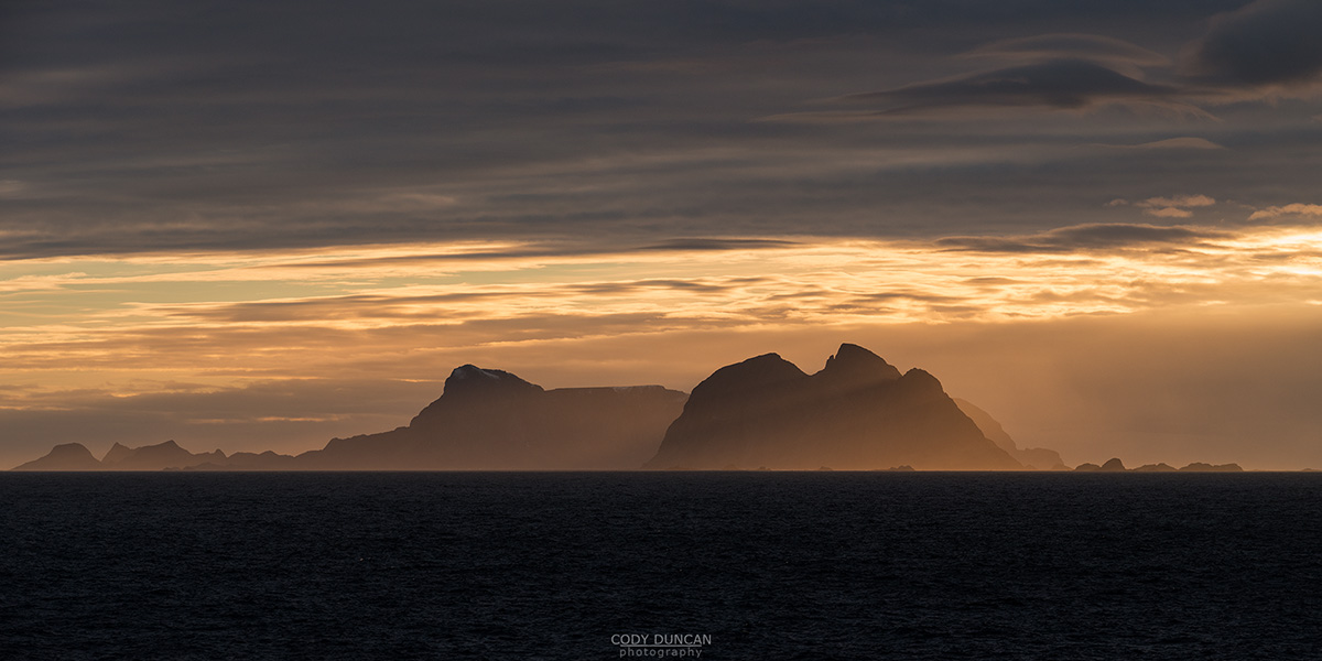 Værøy islands rise over sea while illuminated by winter sunset, Moskenesøy, Lofoten Islands, Norway