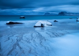 Waves wash over snow covered sand in winter at Myrland beach, Flakstadøy, Lofoten Islands, Norway