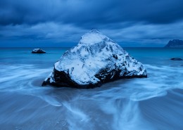 Waves wash over snow covered rock in winter at Myrland beach, Flakstadøy, Lofoten Islands, Norway