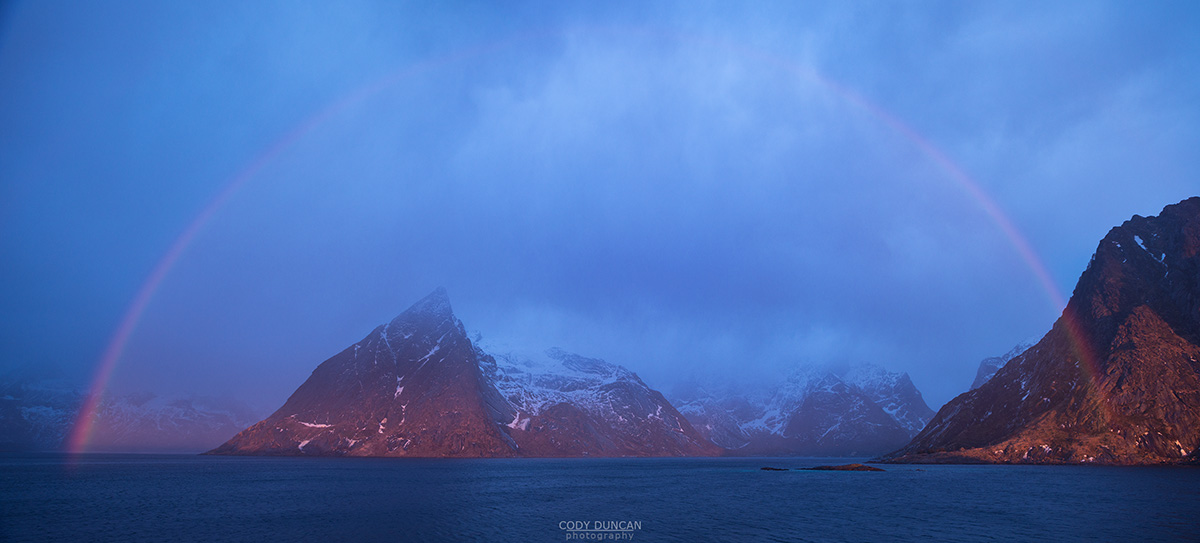 Rainbow forms over Olstind mountain peak and Fjord, Reine, Moskenesøy, Lofoten Islands, Norway