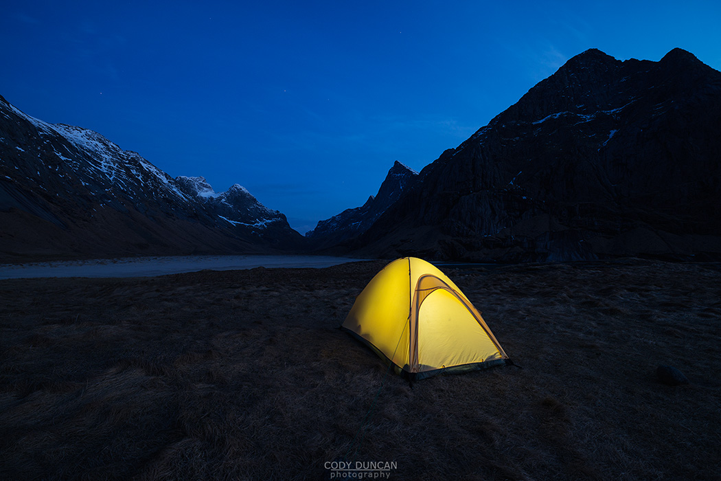 Tent illuminated at night while wild camping at scenic Horseid beach, Moskenesøy, Lofoten Islands, Norway