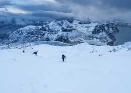 Winter climber ascending steep snow covered slopes towards summit of Hustind, Flakstadøy, Lofoten Islands, Norway