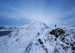 Hiker descending wintry ridge from summit of Mannen mountain peak, Vestvågøy, Lofoten Islands, Norway