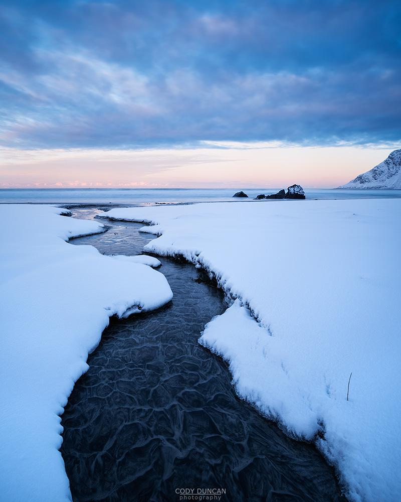 Small river running through snow on Skagsanden beach, Flakstadøy, Lofoten Islands, Norway